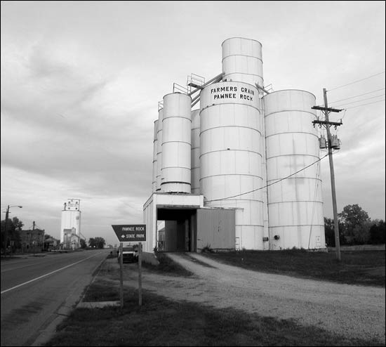 The now-removed steel elevator owned by Farmers Grain stands like a fortress along U.S. 56 in Pawnee Rock. Down the highway, the now-removed feed mill stands in front of the tall white elevator. Photo copyright 2012 by Leon Unruh.