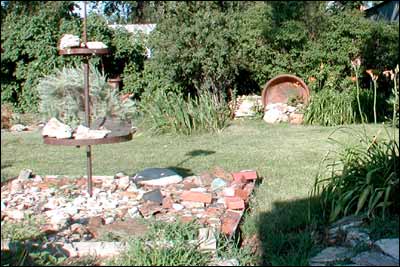 The big iron kettle, retired to a corner of the yard and resting on its side, once held the place of honor where the wagon-wheel sculpture is this photo.