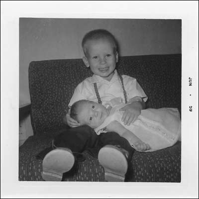 Proud brother and brand-new baby sister on the brown couch with gold-thread embroidery in our basement home on Santa Fe Avenue, 1959.